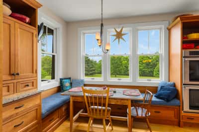 Sun-soaked breakfast nook features built-in seating and panoramic views of lush greenery, perfect for morning coffee.