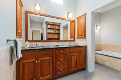 Spacious primary bathroom featuring rich wood cabinetry, ample storage, dual vanities, and a relaxing soaking tub.
