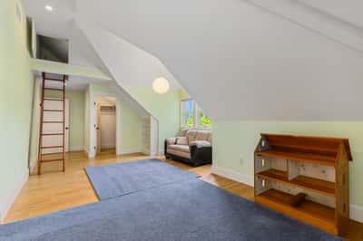 Bright, versatile attic space featuring a cozy sitting area, ladder access, and ample natural light.