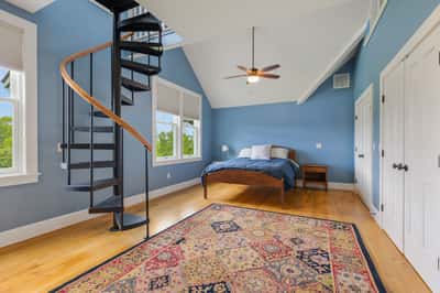 This spacious bedroom features a unique spiral staircase, large windows, and captivating natural light throughout.