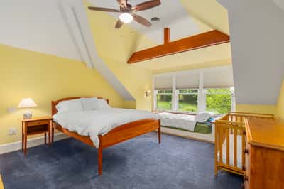 Bright and airy bedroom features vaulted ceilings, large windows, and a cozy sitting area with nature views.
