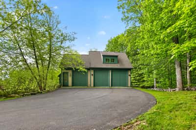 Nestled among lush greenery, this unique property features a spacious driveway and distinctive architecture.