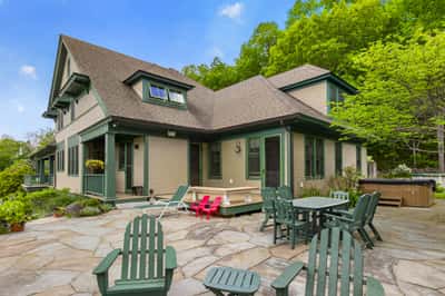 Spacious home with inviting patio, lush greenery, and nearby hot tub, perfect for entertaining and relaxation.