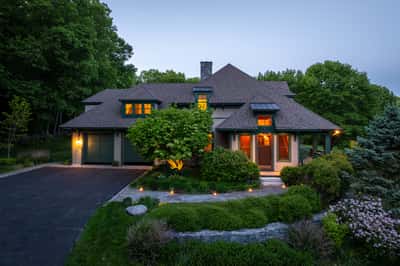 This inviting home features a spacious layout, lush landscaping, and warm exterior lighting for a welcoming atmosphere.