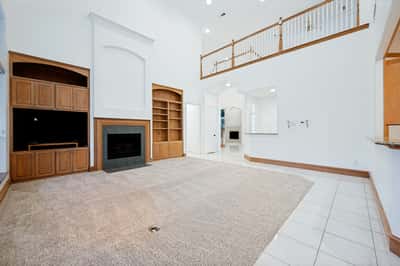 Spacious living area with high ceilings, built-in shelving, and an inviting fireplace, perfect for entertaining.