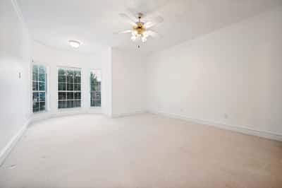 Bright, spacious room with large windows and a ceiling fan, ready for your personal touch.