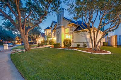 This striking home features impressive architecture, lush landscaping, and warm evening ambiance in a desirable neighborhood.