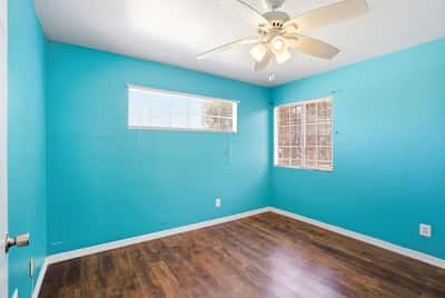 Brightly painted room with ample natural light, featuring a ceiling fan and modern wood flooring.