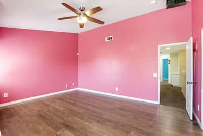 Bright, vibrant room with a unique pink accent wall and modern ceiling fan, perfect for personalization.