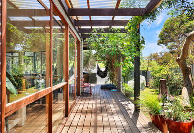 This inviting covered deck offers a perfect blend of indoor-outdoor living, surrounded by lush greenery.