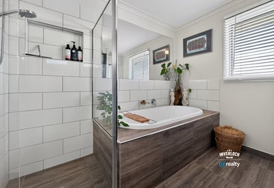 Modern bathroom featuring a spacious tub, glass shower, and organized space with natural light.