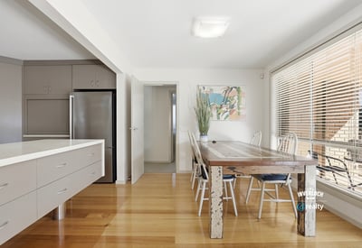 Bright and airy dining space featuring a rustic wooden table, modern kitchen amenities, and abundant natural light.