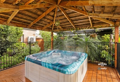 Relax in this private hot tub surrounded by lush landscaping under a rustic wooden pergola.