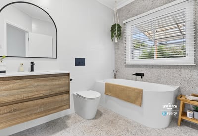 Modern bathroom featuring a freestanding tub, large mirror, and ample natural light from the window.