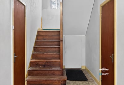Bright entryway featuring a wooden staircase and dual access doors, perfect for welcoming guests.