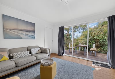 Bright living area featuring large sliding doors that open to a private outdoor deck surrounded by greenery.