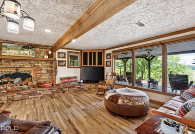 Spacious living area features wood accents and large windows overlooking a picturesque outdoor landscape.