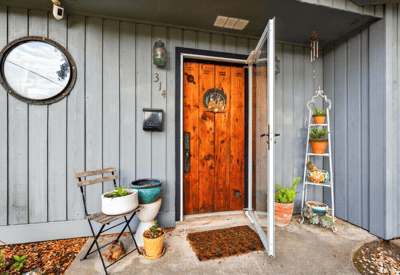 Inviting entryway featuring a striking wood door, potted plants, and a cozy seating area.