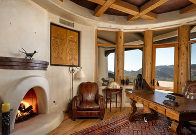 A custom kiva-style fireplace anchors this intimate office, surrounded by artisanal finishes and panoramic desert views. This thoughtfully curated space offers sophistication and warmth for working or relaxing in style.