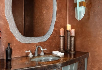 This artistic powder room makes a bold impression with a handcrafted metal vanity and mirror ensemble. Rich wall finishes and designer sconces create a luxurious ambiance perfectly blending modern design with southwestern charm.