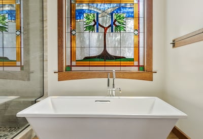 Relaxing soaking tub framed by decorative stained glass and warm wood trim. This peaceful bathroom retreat blends artistry with luxury finishes.