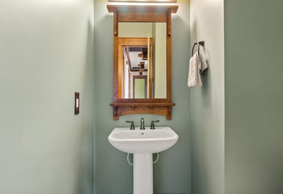 Designer half bath with pedestal sink, custom mirror, and handcrafted wood accents. A polished space that adds charm and convenience for visitors.