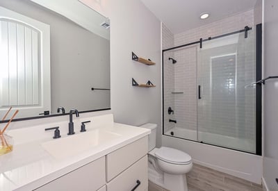 This modern hall bathroom showcases a tiled tub/shower combo, black framed glass doors, and a crisp white vanity for a polished look.