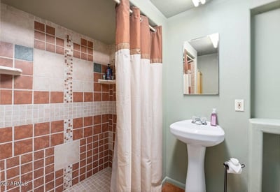 Full bathroom featuring tile shower walls, pedestal sink, and practical layout that complements the home s rustic design.