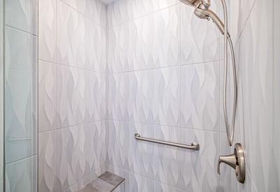 The shower s eye-catching tilework and sleek glass surround add elegance and modern flair to this beautifully updated bathroom.