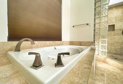 Luxurious soaking tub surrounded by elegant marble tile and designer fixtures, creating a tranquil retreat within this Scottsdale home.