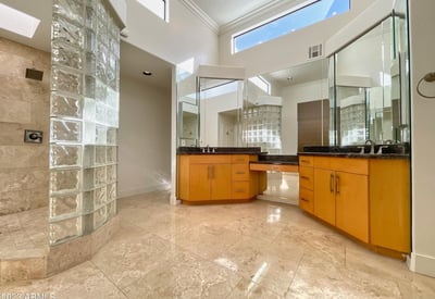 Spacious bathroom with high ceilings, glass-block shower, and granite vanities. Elegant design and natural light define this luxurious space.