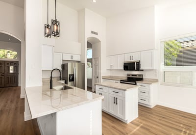 Updated Scottsdale kitchen featuring a spacious island, sleek quartz-style counters, white cabinetry, and stainless steel appliances. Modern pendant lighting and vaulted ceilings enhance the contemporary open layout.