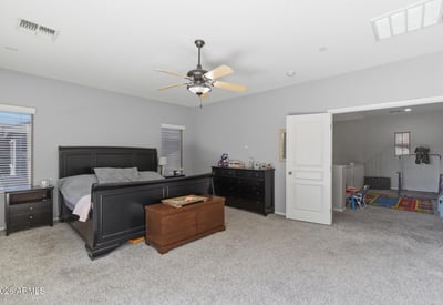 Generous primary suite featuring plush carpeting, large windows, ceiling fan, and ample space for bedroom furniture, creating a peaceful retreat in this Queen Creek property.