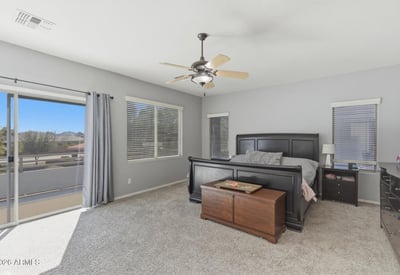 Beautiful primary bedroom with sliding glass doors leading to a private balcony, allowing fresh air and scenic neighborhood views.