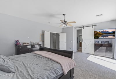 Elegant primary bedroom with barn-style sliding door access to the bathroom, spacious layout, and soft carpeting for a comfortable and stylish retreat.