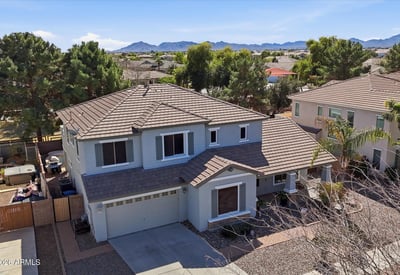 Elevated drone view showing the home's position within the neighborhood with distant mountain scenery and surrounding residential streets in Queen Creek.