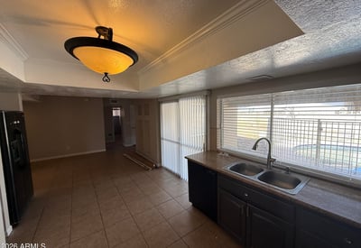 Kitchen area with double sink, tile counters, and rich cabinetry. Natural light from the wide window brightens the room while offering a glimpse of the pool area outside.