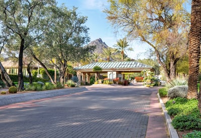 Inviting gated entry with lush landscaping, mature trees, and desert accents, enhancing curb appeal in this Phoenix community.