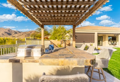Scottsdale backyard kitchen with stone counters, grill, and seating under pergola, ideal for gatherings and outdoor dining.