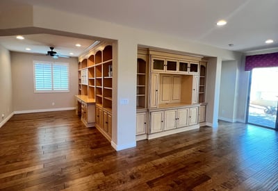 Open great room with stunning custom entertainment cabinetry, built-in office shelving, upgraded wood flooring, recessed lighting, and plantation shutters creating an elegant and highly functional living space.