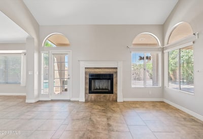 This welcoming family room features a wood-burning fireplace, soaring ceilings, and French doors leading to the covered patio. The spacious layout creates a comfortable gathering place with easy indoor-outdoor flow.