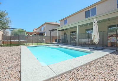 Private backyard featuring a sparkling pool, covered patio, removable pool fence, and lush lawn. A fantastic outdoor space for entertaining, relaxing, and enjoying Arizona's sunny climate.