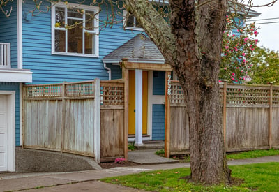 This inviting home features a unique yellow door, framed by a well-maintained wooden fence and inviting landscaping.