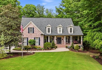 This beautiful home features a welcoming front porch, expansive lawn, and lush surrounding greenery for privacy.