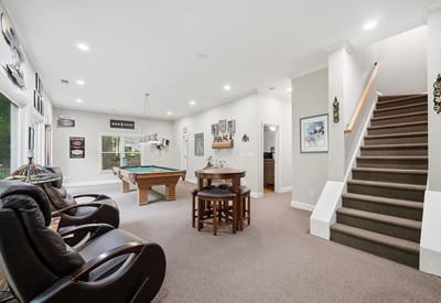 Spacious recreational area featuring a pool table, cozy seating, and an inviting staircase to the upper level.