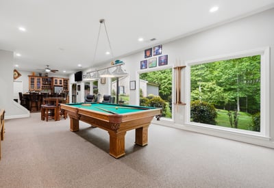 Spacious recreational room featuring a billiard table, large windows, and scenic views of the landscaped yard.