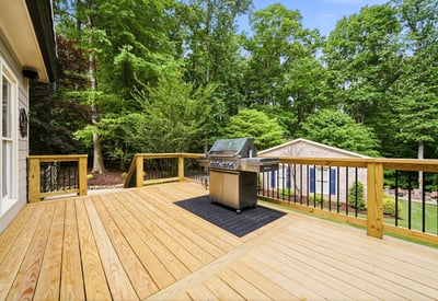 Spacious deck featuring a built-in grill, perfect for outdoor entertaining amid a lush, wooded backdrop.