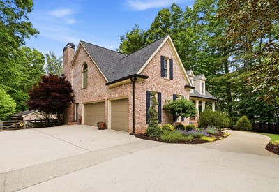 Stunning brick home with a spacious driveway, surrounded by lush landscaping and mature trees.