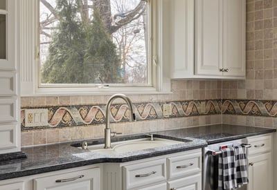 Modern kitchen featuring sleek countertops, ample cabinetry, and a window overlooking a lush outdoor space.
