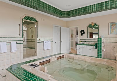 Spacious bathroom featuring a luxurious jetted tub, large walk-in shower, and distinctive green tile accents.